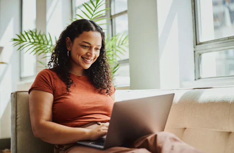 A woman relaxing on her sofa, using a laptop to access support at home.
