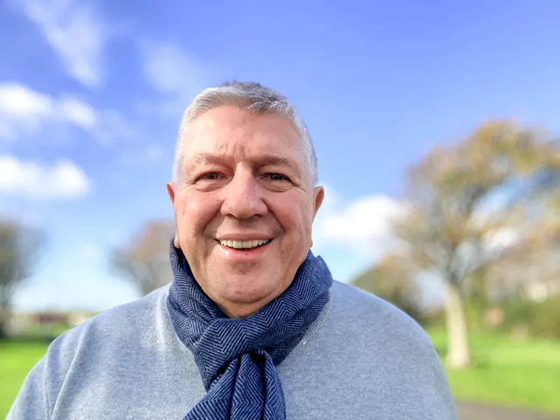 A smiling older man wrapped up warm, enjoying a walk in the park.