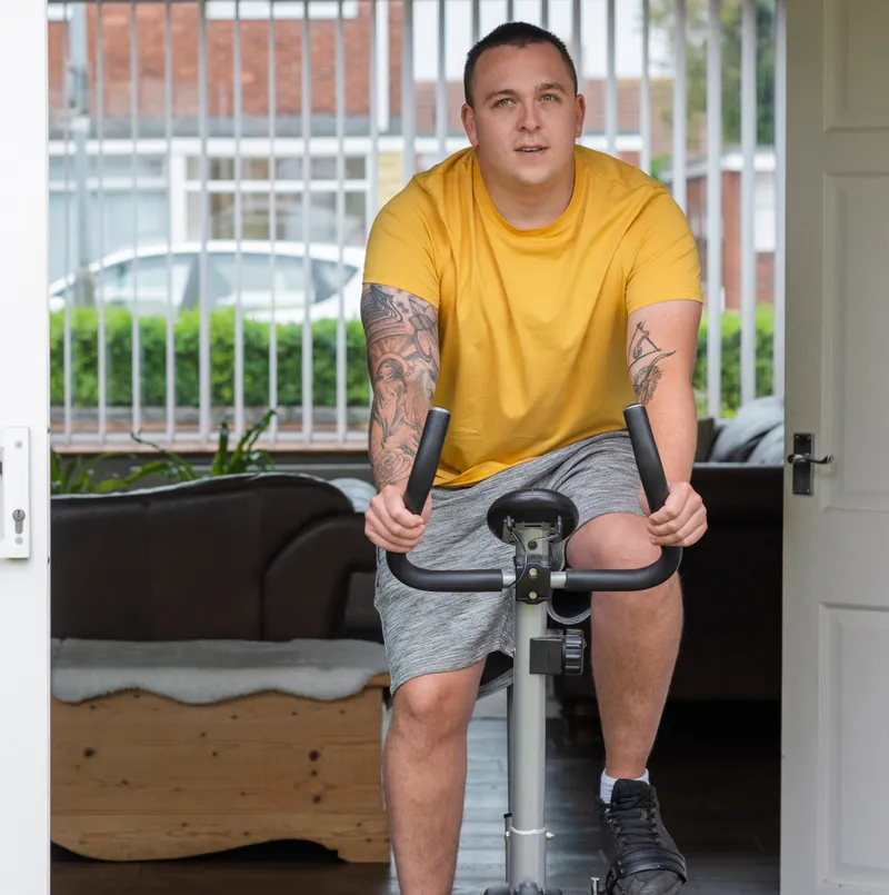 A man keeping active on a stationary exercise bike by his open patio doors at home.