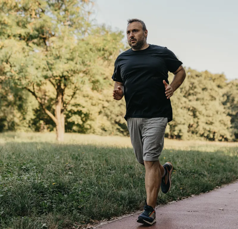 A man jogging along a tree-lined path in a park.